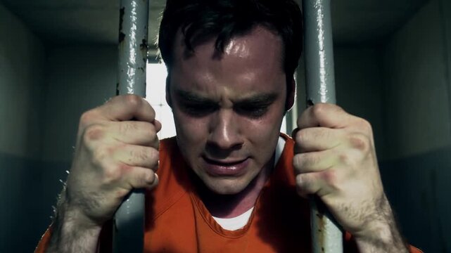 Desperate male inmate screaming and gripping bars in prison cell. Close-up shot with camera moving forward.