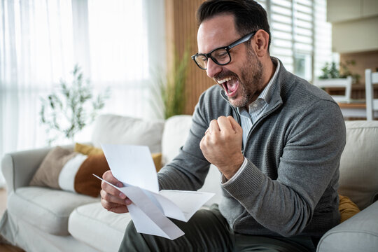 Happy man celebrating good news reading letter at home