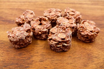Milk chocolate clusters isolated on a wooden background. A delicious treat made of milk chocolate with cereal flakes and caramel pieces.