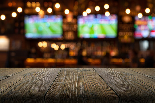 A natural wood table and a blurred background of a sports bar with screens and football broadcasts