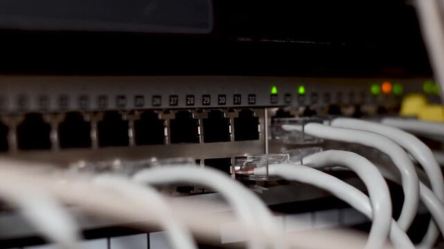 Server room rack with network cables. Network cables connect to server rack ports with blurry bokeh lights in the background. A close-up of a network rack with multiple Ethernet cables connected to it