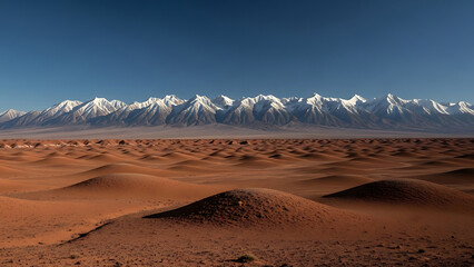 Vast orange desert dunes stretch towards snow-capped mountains under a clear blue sky sand