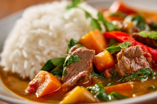 A close-up of spicy Guinean Maafe (peanut stew), rich with tender meat and vegetables, served with fluffy white rice.