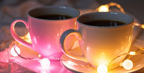 Cozy evening with two warm coffee cups surrounded by colorful string lights on a table