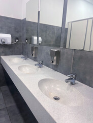 Modern restroom interior with stone gray tiles. Contemporary interior of public toilet. minimal interior with white tiles, round mirrors. Perspective of men's restroom. commercial bathroom. 