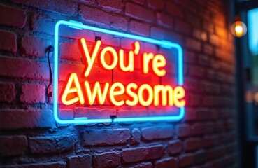Glowing neon sign with Youre Awesome text on brick wall. Bright electric lights provide positive affirmation and urban decor. Modern encouragement message glows in blue and red.