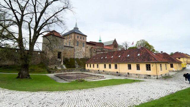 akershus fortress stone towers ramparts behind yellow barracks building cobblestone paths lawns trees visitors appear oslo norway wide view historic citadel 