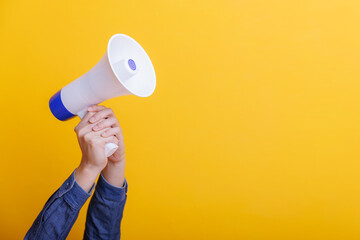 Hand of businessman holding megaphone or bullhorn against yellow background