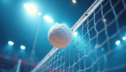 White volleyball sails over net in indoor sports arena. Bright stadium lights shine on ball during intense match. Pro game play unfolds on court floor.