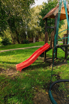 Playground with red slide, placed in a green park for children's leisure and physical activity.