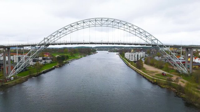 symmetrical steel arch bridge glomma river rippling water apartments neighborhoods stretch into distance fredrikstad norway wide drone view urban infrastructure 