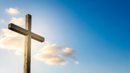 Wooden Christian cross standing tall under a clear blue sky with soft white clouds. Peaceful religious landscape representing resurrection, grace, and spiritual belief.