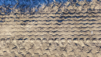 Close-up overhead view of deep tire tracks imprinted in dry, dusty earth with hints of frost