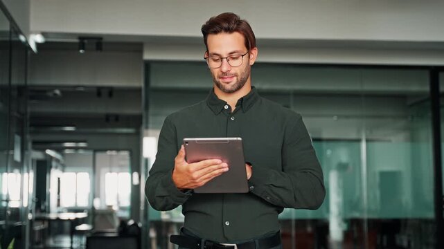 Focused European young businessman entrepreneur working on touchscreen computer device. Latin hispanic ceo business man ceo manager using tablet pad computer in office, looking at screen typing