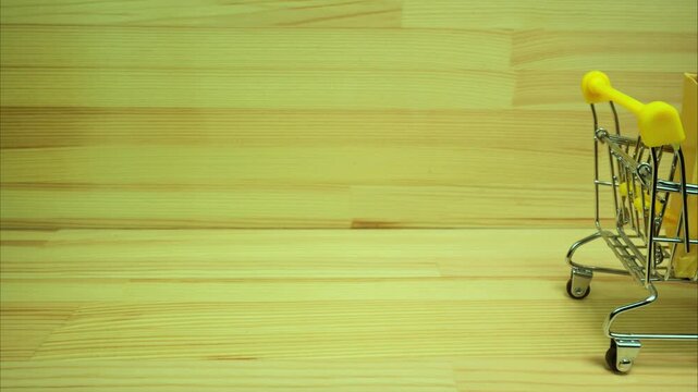 Mini shopping carts with gifts, packages and books moving on wooden background. Stop motion 