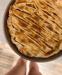 Homemade pie in baking dish seen from above, close-up top view, with part of a young woman legs visible, cozy home cooking scene, female chef preparing dessert, lifestyle photography