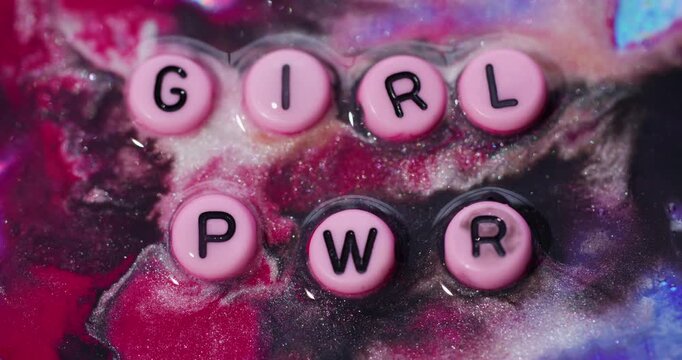 Girl pwr word. Glitter ink. Defocused pink blue red color sparkling particle black power letters feminism texture on abstract acrylic art background.