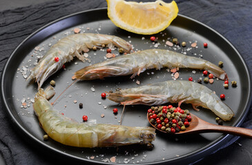 Raw shrimp with spices on a black round plate
