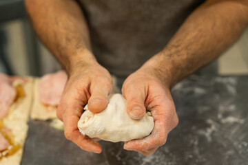 Hands of professional baker folding and sealing stuffed dough, artisanal baking process and craftsmanship.