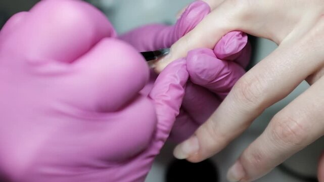 Professional close-up footage of a skilled nail technician wearing protective rubber gloves removing cuticle with professional cutters,  performing a precise manicure on a female client. 