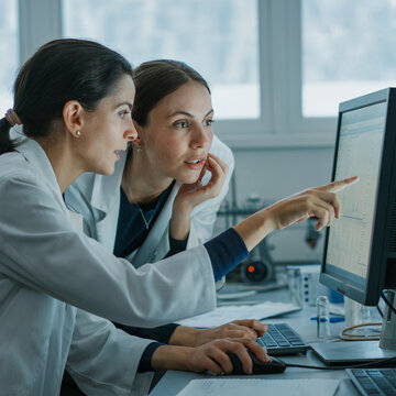 Dos cient&iacute;ficas en batas de laboratorio analizando datos en un monitor de computadora