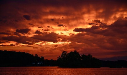 A dramatic fiery sunset ignites the evening sky over a peaceful lake.
