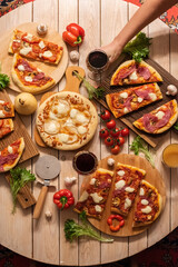 Pizzas with meat, mushrooms and pears on a round table and a woman's hand with glasses of wine