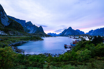 Obraz premium Autumn sunset in Reine, Lofoten Islands, Norway, with dramatic mountains, calm waters, and traditional houses along the shore.