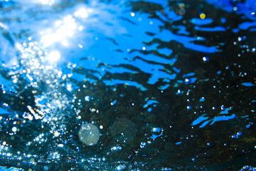 Abstract underwater view of sunlight shining through deep blue water with bubbles.