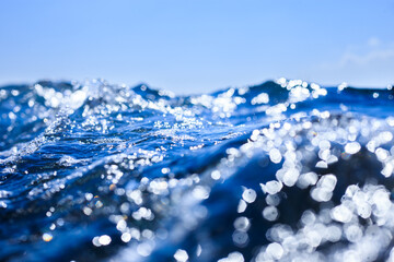 Close-up of a sparkling blue ocean wave in bright sunlight with a clear sky background. Bright sun creates sparkling reflections and beautiful bokeh.
