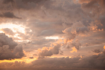 Fototapeta premium Cumulus clouds fill the sky, displaying a blend of orange, gold, and warm twilight hues, creating an atmospheric background texture with soft light and shading