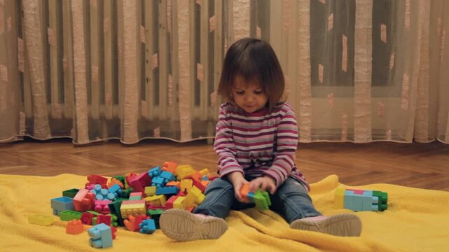 Hyperactive toddler girl building blocks on floor while playing in her room