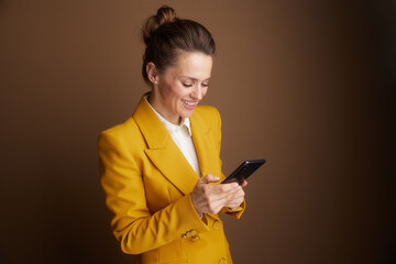 A smiling businesswoman in a yellow blazer is engrossed in her smartphone, highlighting digital connectivity and efficient communication in the professional world.