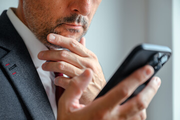 Pensive executive checking mobile phone, hand on chin in serious reflection at workplace.