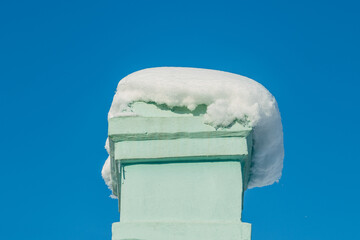 Pale green chimney top with thick snow cap against clear blue sky