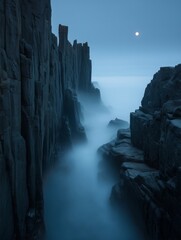Dramatic and lonely sea stacks and ethereal mist cliffs emerging from a thick, flowing fog bank during the silent blue hour before sunrise