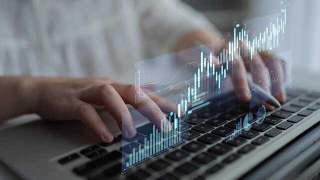 A close-up view of hands typing on a laptop as digital financial graphs and analytics emerge, representing the intersection of technology and data analysis in business. Scalp - Powered by Adobe