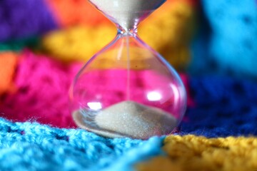Hourglass sand glass as symbol of passing time and crocheted granny square blanket beautiful cozy handmade photo concept of time for relax hobby handiwork leisure autumn winter vibe  