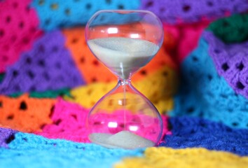 Hourglass sand glass as symbol of passing time and crocheted granny square blanket beautiful cozy handmade photo concept of time for relax hobby handiwork leisure autumn winter vibe  