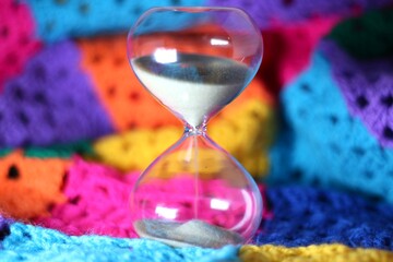Hourglass sand glass as symbol of passing time and crocheted granny square blanket beautiful cozy handmade photo concept of time for relax hobby handiwork leisure autumn winter vibe  