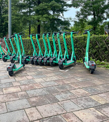 row of electric scooters are parked neatly on paved surface, ready for use. green scooters, providing an eco-friendly transport option. convenience and eco-friendliness of sustainable urban transport.