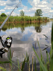Fishing rod with reel casting into calm pond water surrounded by tall grass and nature. the concept of quiet fishing in the river.