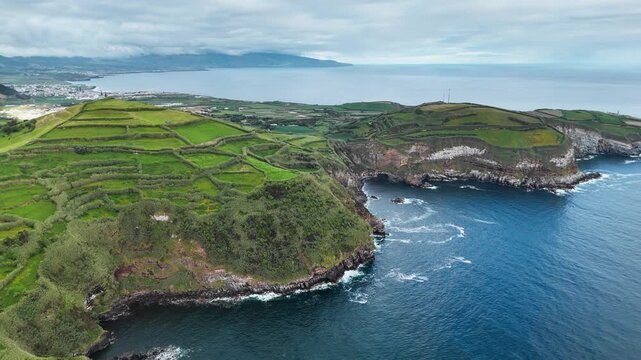 Green agricultural cliffs above Atlantic Ocean with patchwork farmland and rugged coastline in Azores Islands. Aerial view