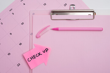 Medical check up reminder. Clipboard and pen on pink calendar background