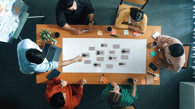 A top-down view of a dynamic team engaging in a creative meeting, surrounded by laptops, notes, and visual materials, fostering collaboration and innovation. Raster