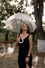 Woman, rain, umbrella. Serene woman enjoying refreshing drizzle with a clear umbrella on a wet park path.