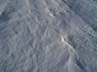 Close-up of wind-shaped snow texture forming natural frost patterns. Abstract winter background with icy surface, blue tones and fine crystalline details, ideal for seasonal and minimalist designs