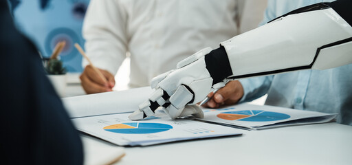 A futuristic robot arm is engaged in a business meeting, analyzing charts and graphs while team members collaborate in a modern office setting.Noogenesis