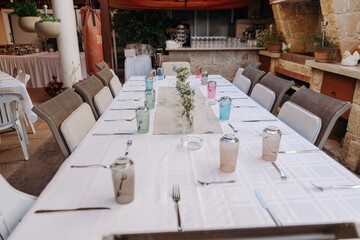 Long dining table set on an outdoor terrace with colored glasses and wildflowers. Casual family gathering or event setup in a rustic patio