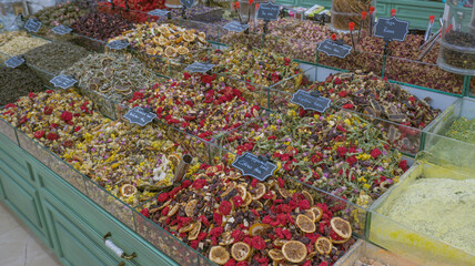 Colorful display of dried fruits, herbs, and spices in a market stall with labeled containers.